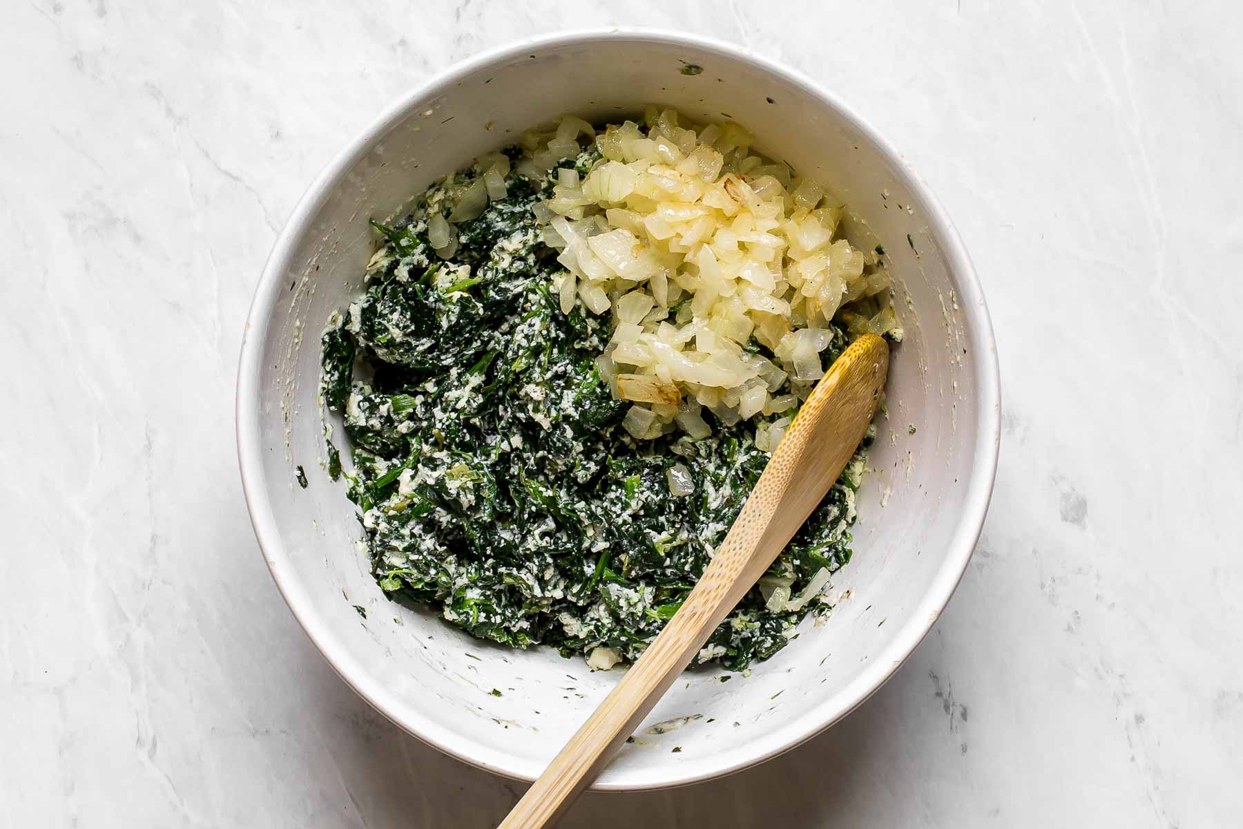 Spinach and cooked onions in a white bowl.