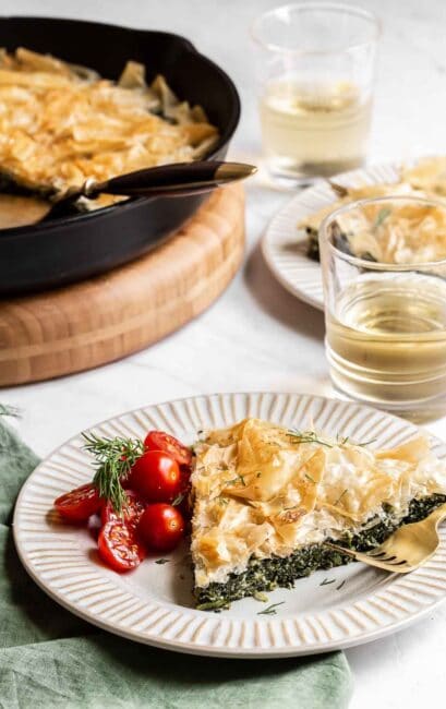 Skillet spanakopita slice on plate with cherry tomatoes aside.