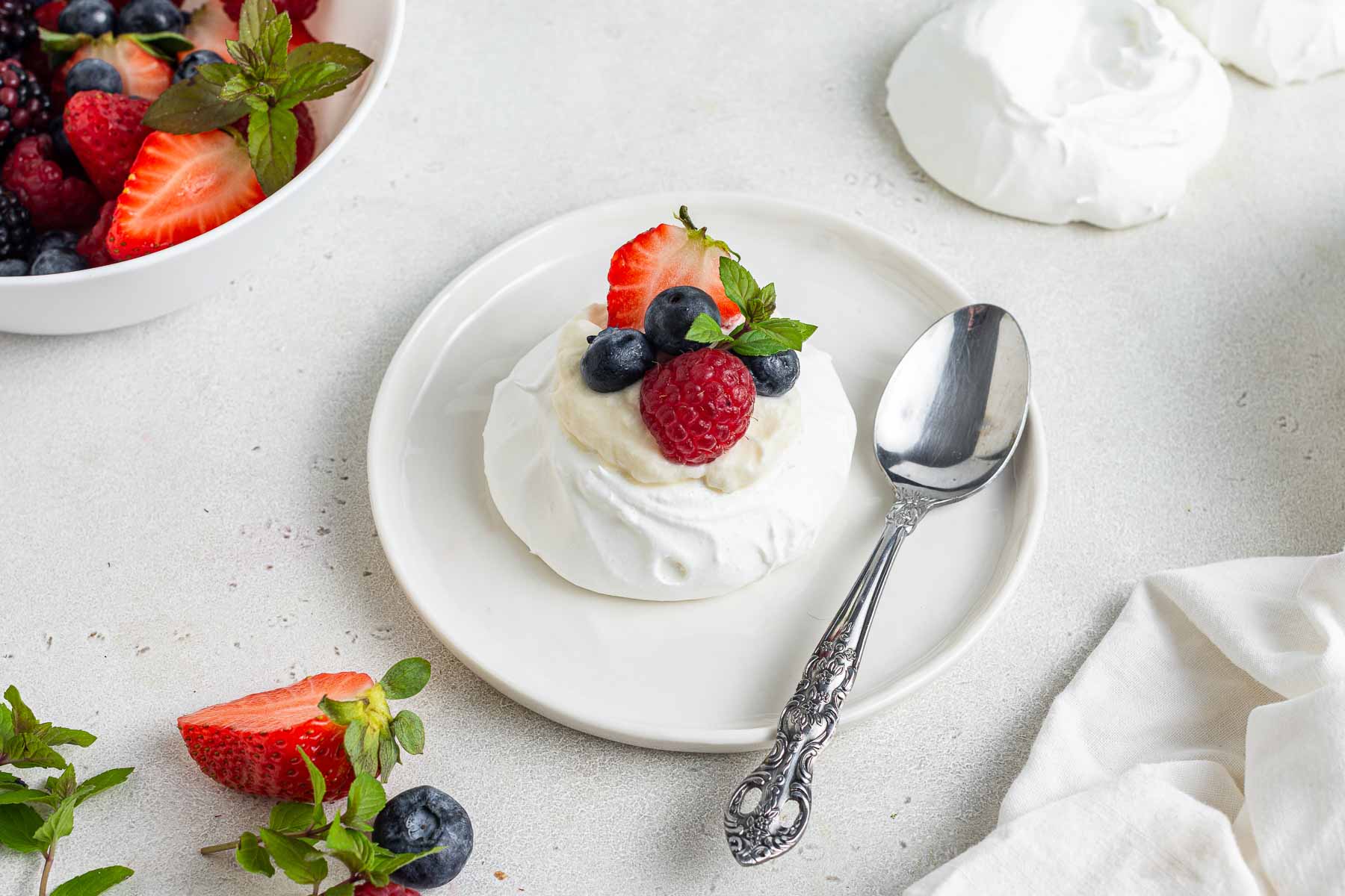 Mini pavlova on plate with fresh whipped cream and berries.