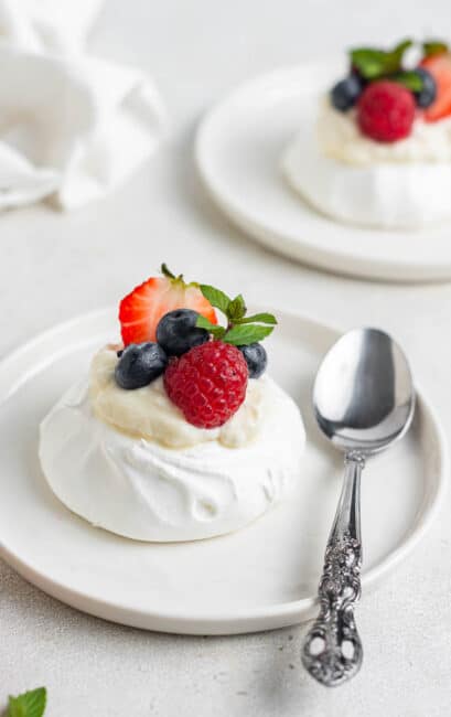 Mini pavlova on white plate with fresh berries on top.