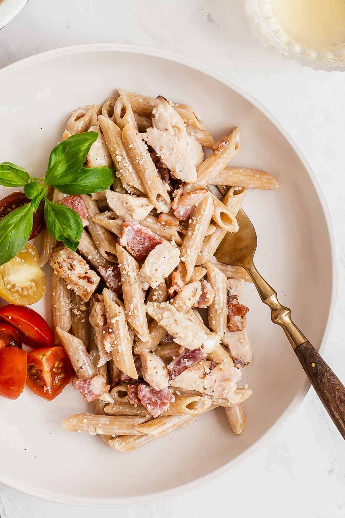 overhead shot of creamy pasta on a plate with bacon chicken and fresh tomatoes