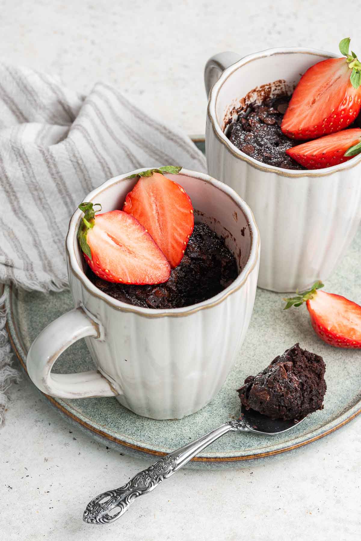 Two coffee cups with a dark treat topped with strawberries and spoon on side.