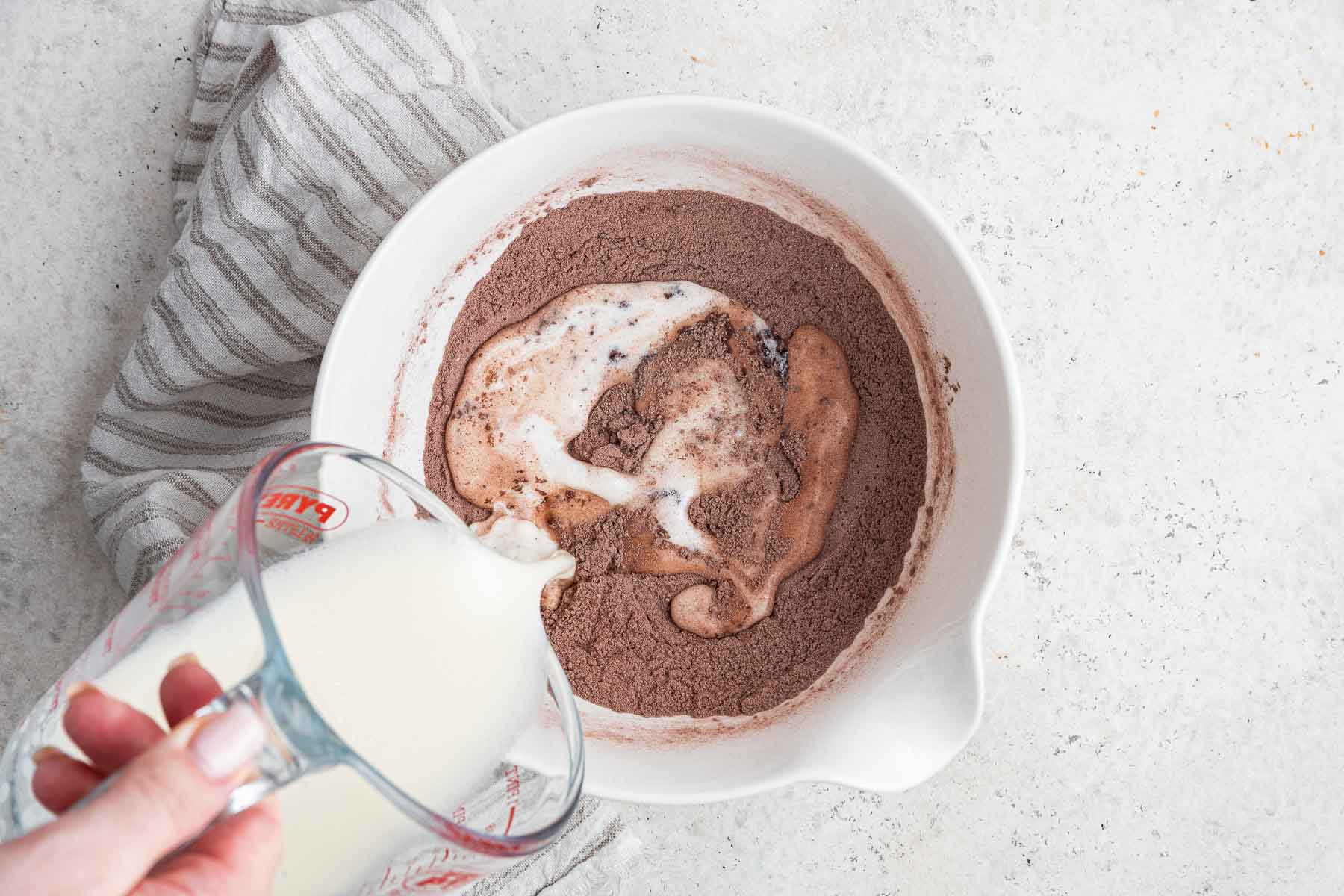 Pouring milk into a cocoa powder mixture in a white bowl.