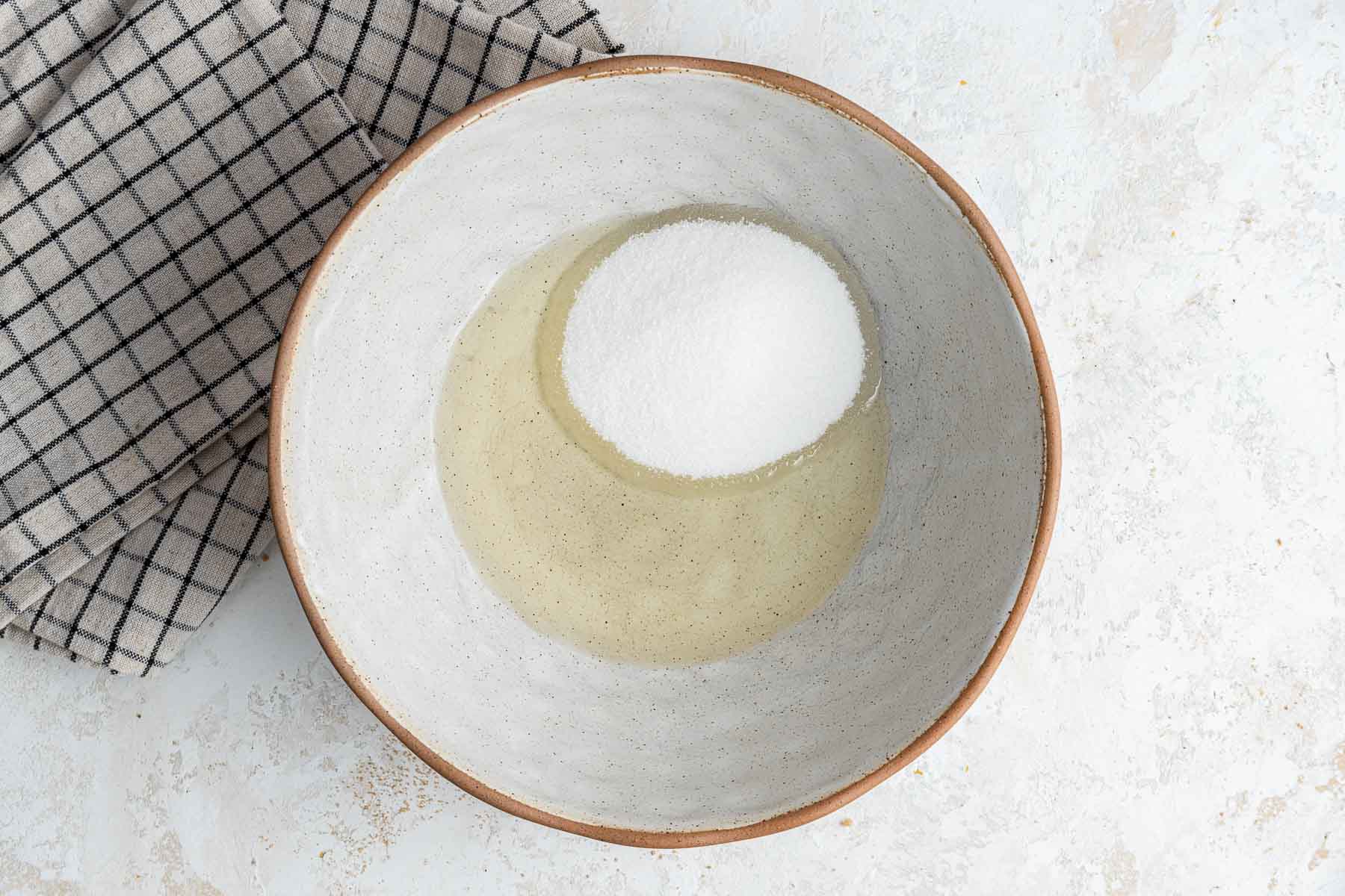 Oil and sugar in small bowl with kitchen towel on side.