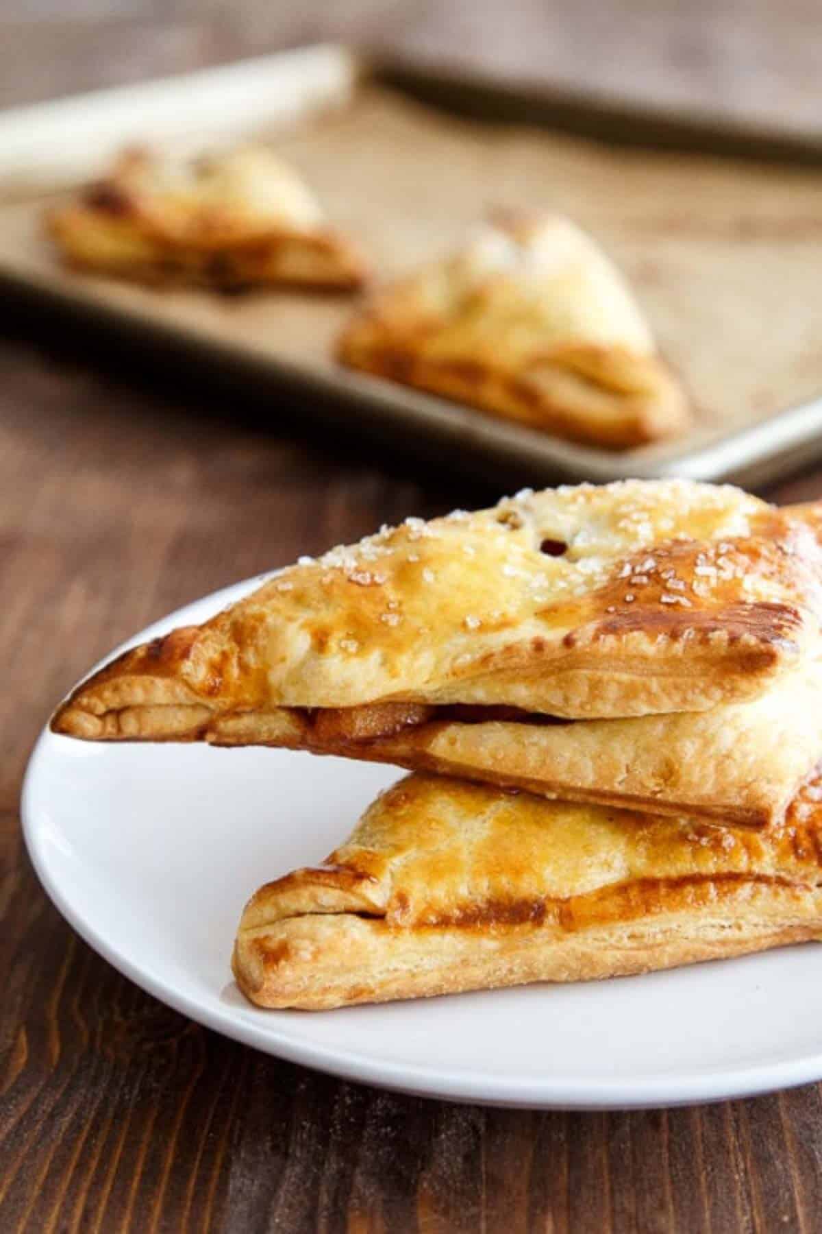 Two apple turnovers stacked on a white plate with cooked apples spilling out.