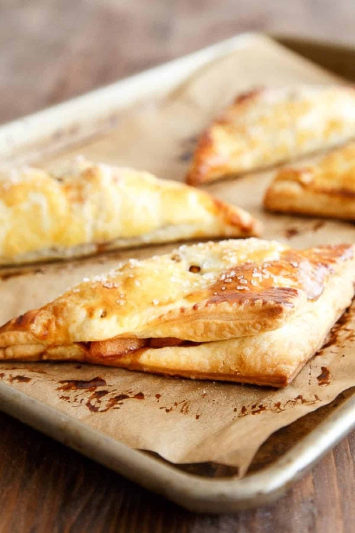 Freshly cooked apple turnovers on baking sheet with brown parchment paper.