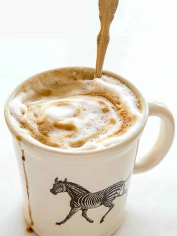 White mug with zebra on it filled with foamy gingerbread latte and a spoon.