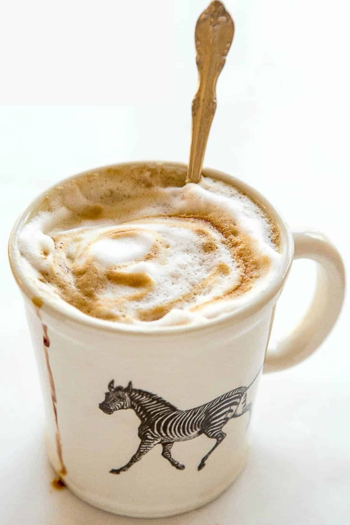 Mug with zebra filled with foamy gingerbread latte and a spoon on the side.
