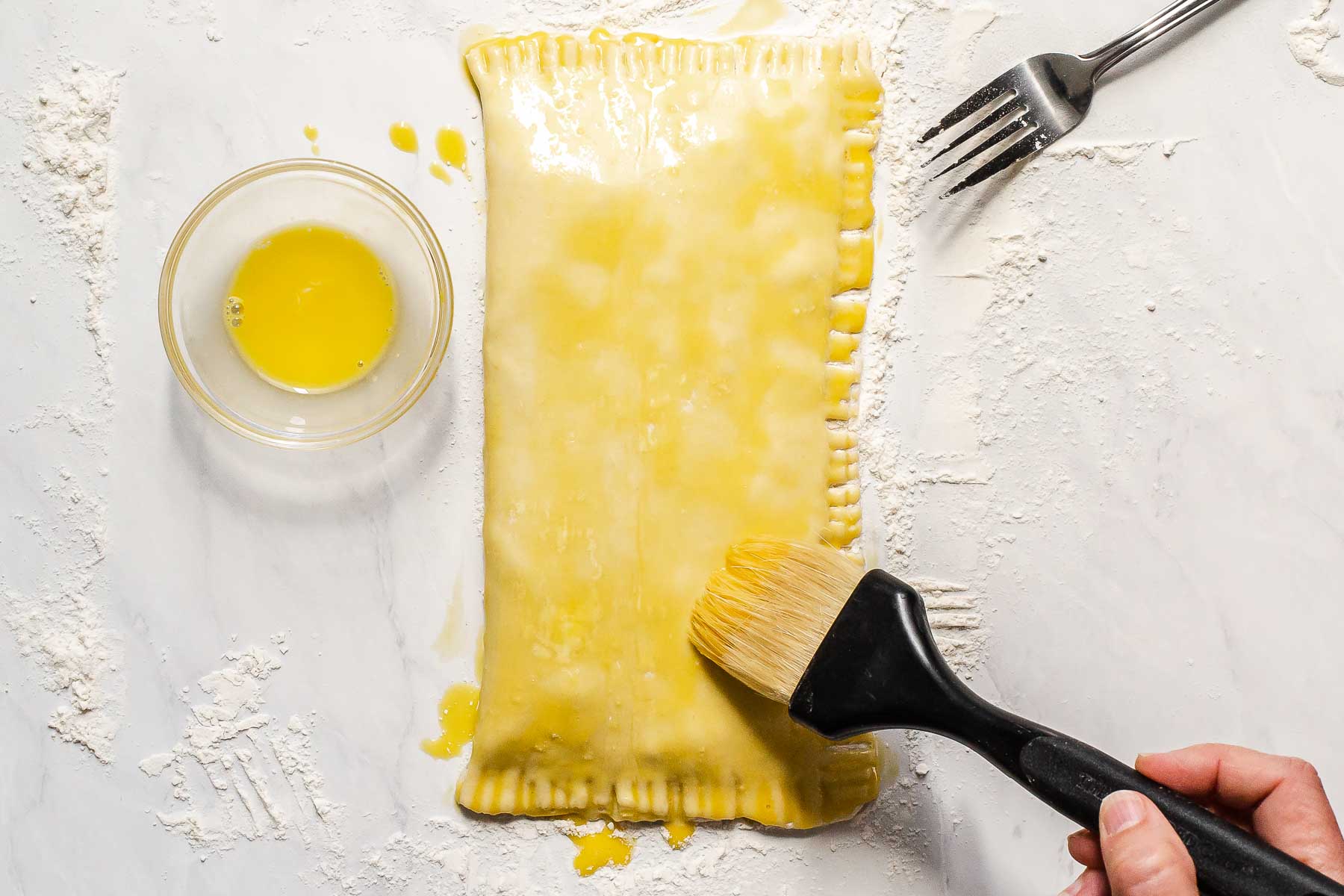 Puff pastry being brushed with beaten egg yolk.