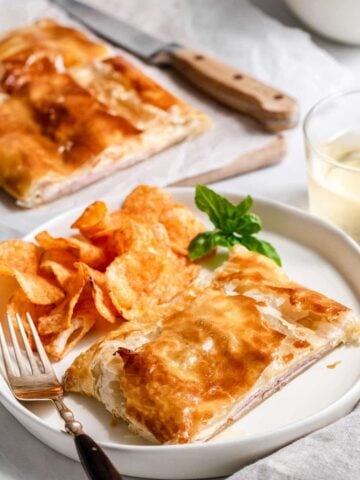 Ham and cheese puff pastry square on a plate with chips.