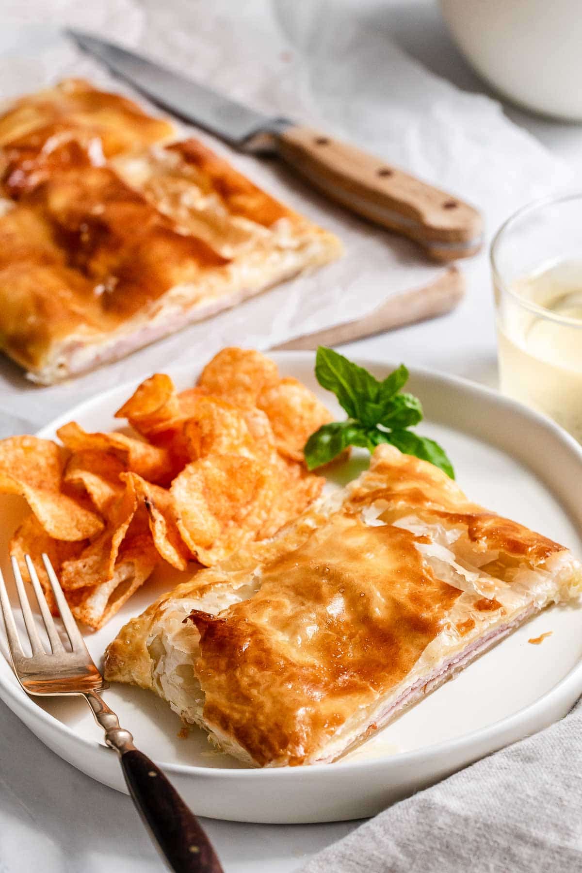 Ham and cheese puff pastry square on a plate with chips.