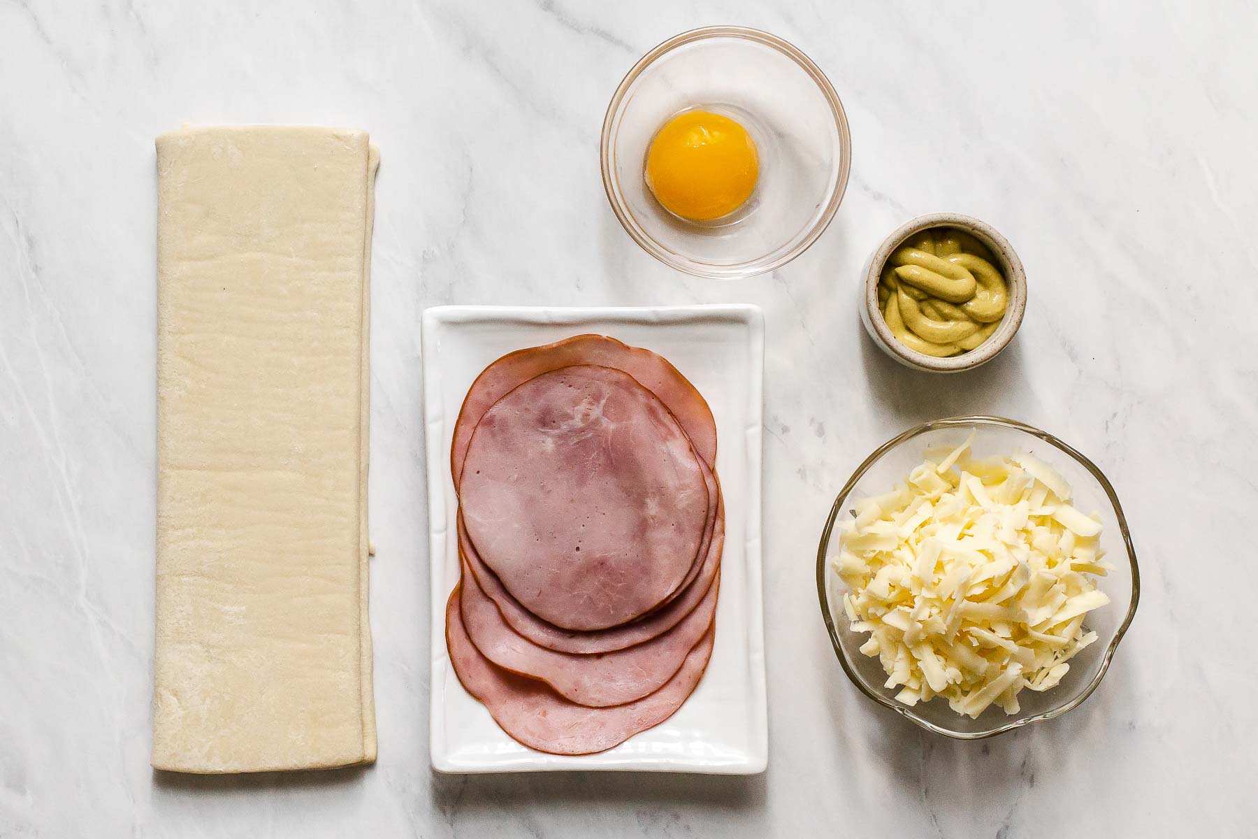 Ham, cheese, pastry, and mustard on a white kitchen table.