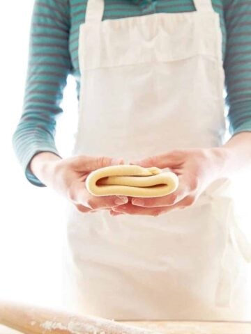 Woman in blue shirt and white apron holding folded puff pastry recipe.