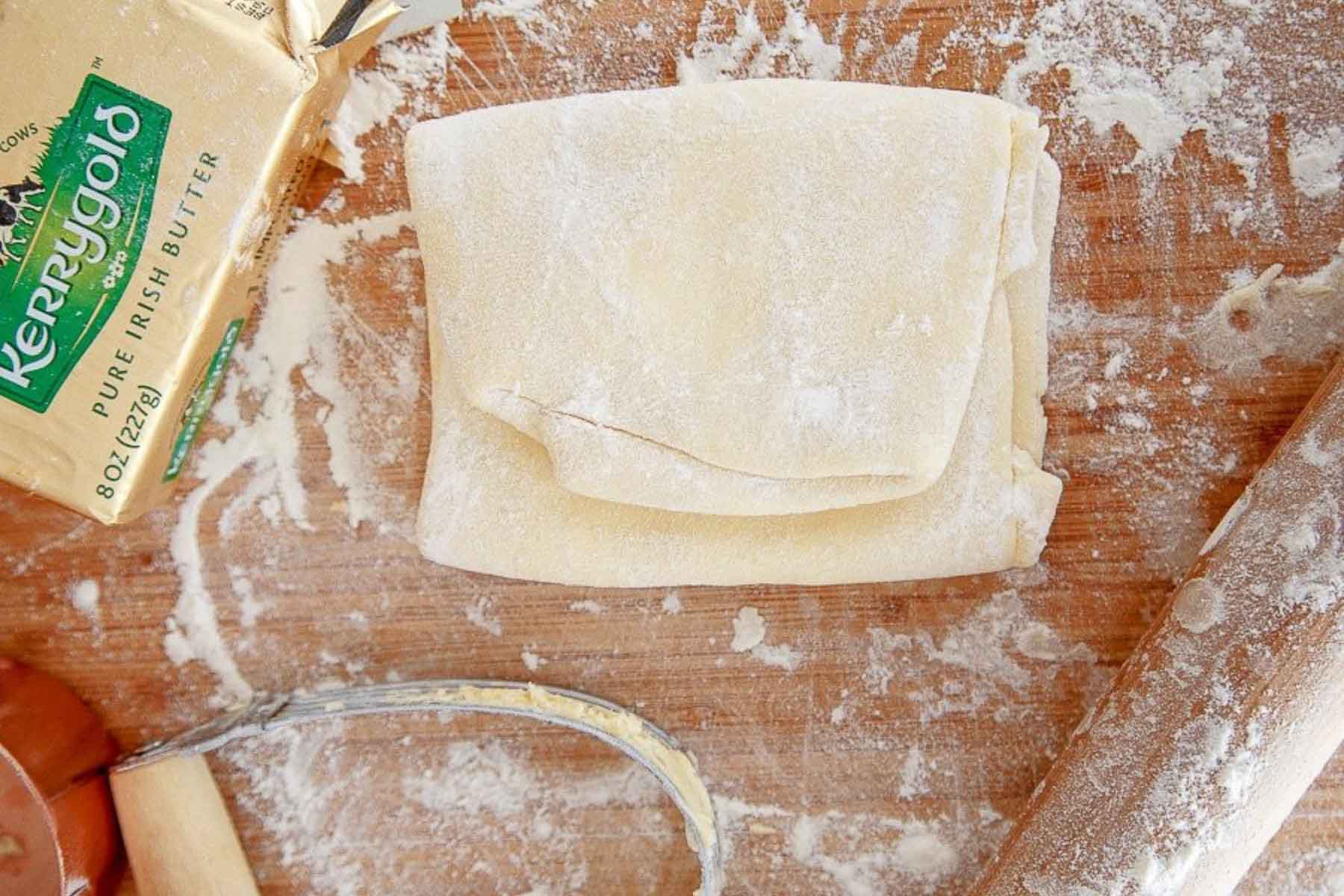 Sheet of homemade puff pastry recipe folded up with butter and pastry blender on side.
