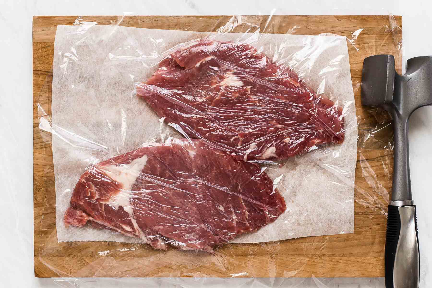 Pork tenderloin cut in half on cutting board covered in plastic.