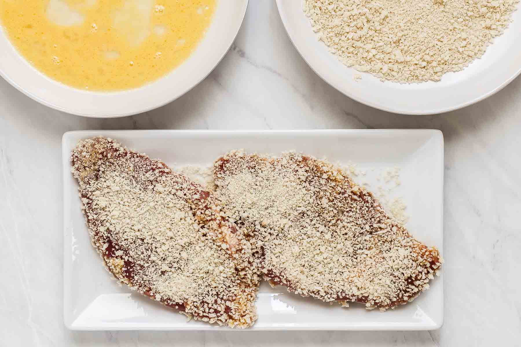 Cutlets dipped in egg and bread crumbs resting on plate.