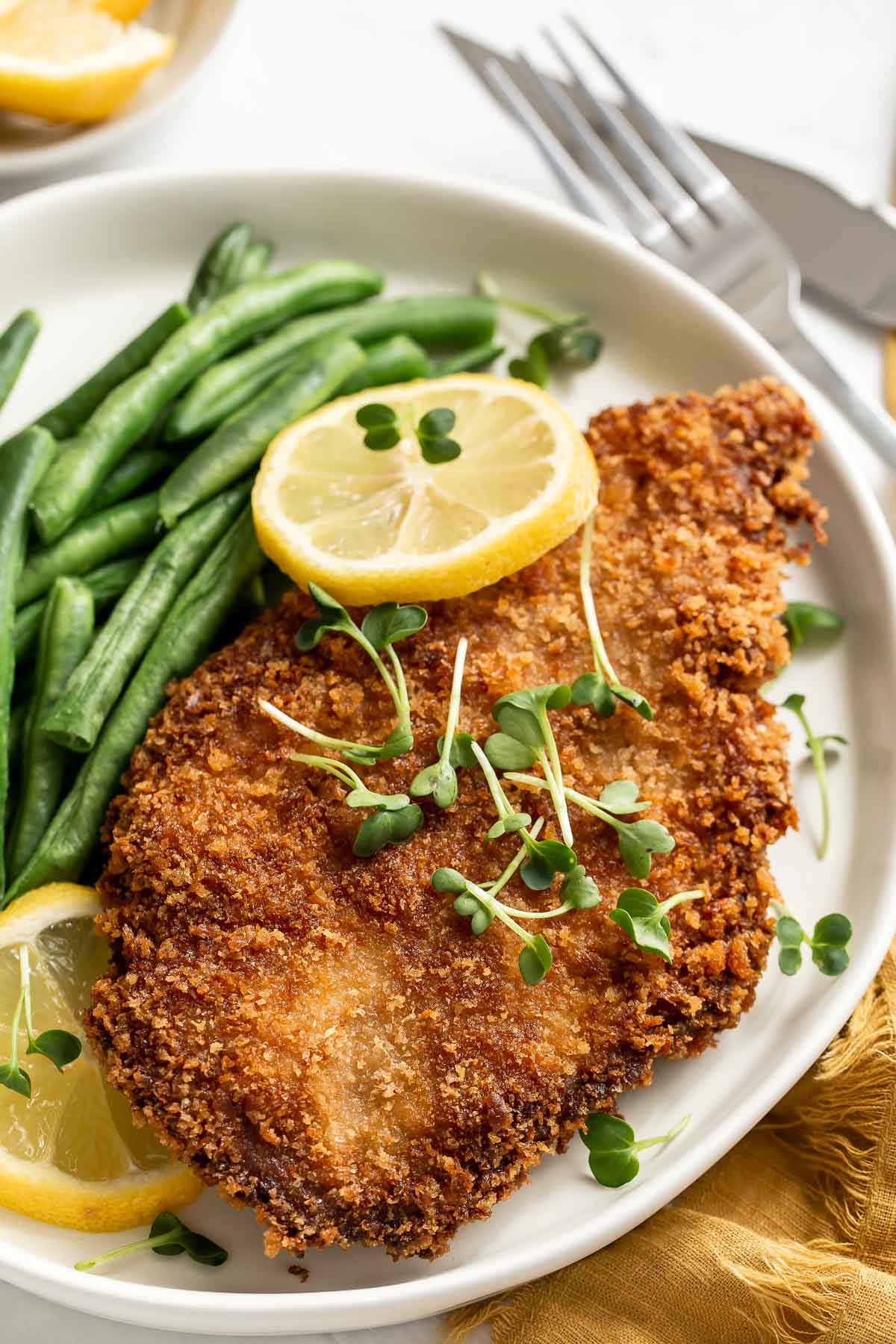 Perfect pork schnitzel on a plate with green beans and lemon slices.