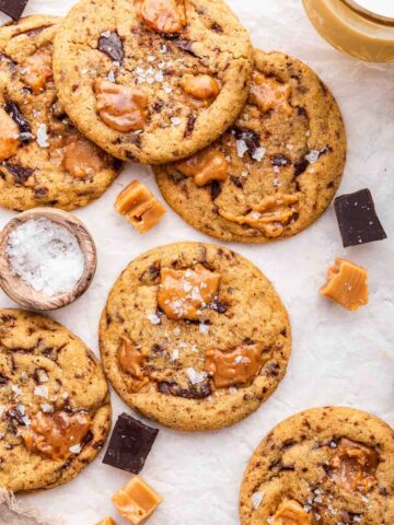 Overhead shot of caramel chocolate chip cookies with bowl of salt on side.