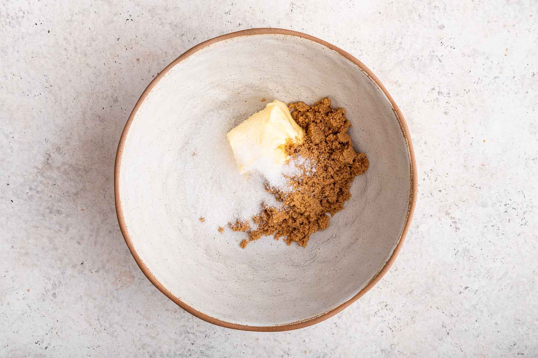 White ceramic bowl with soft butter and two types of sugar.