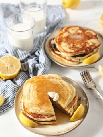 Two plates of lemon pancakes with butter and syrup on top.