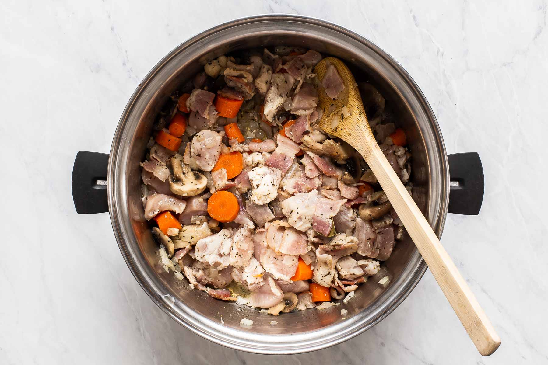 Chicken pieces in vegetables, sautéing in a stock pot.