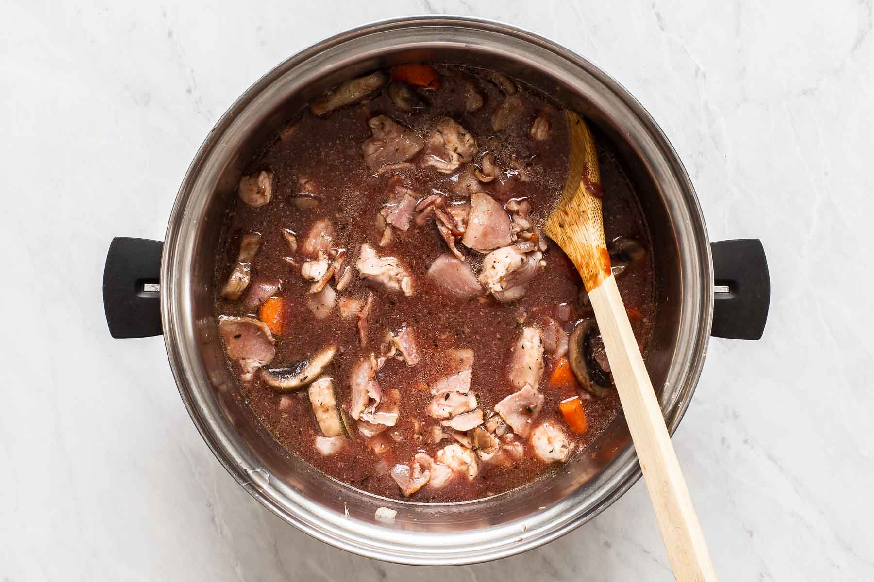 Red wine in a stew pot with vegetables and chicken.