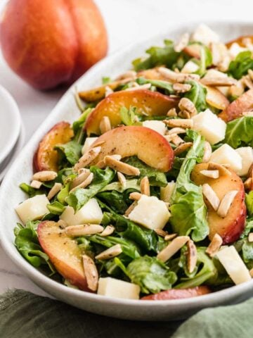 Arugula salad with sliced nectarines on top and almonds.