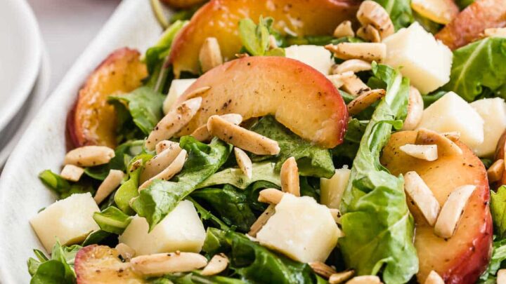 Arugula salad with sliced nectarines on top and almonds.