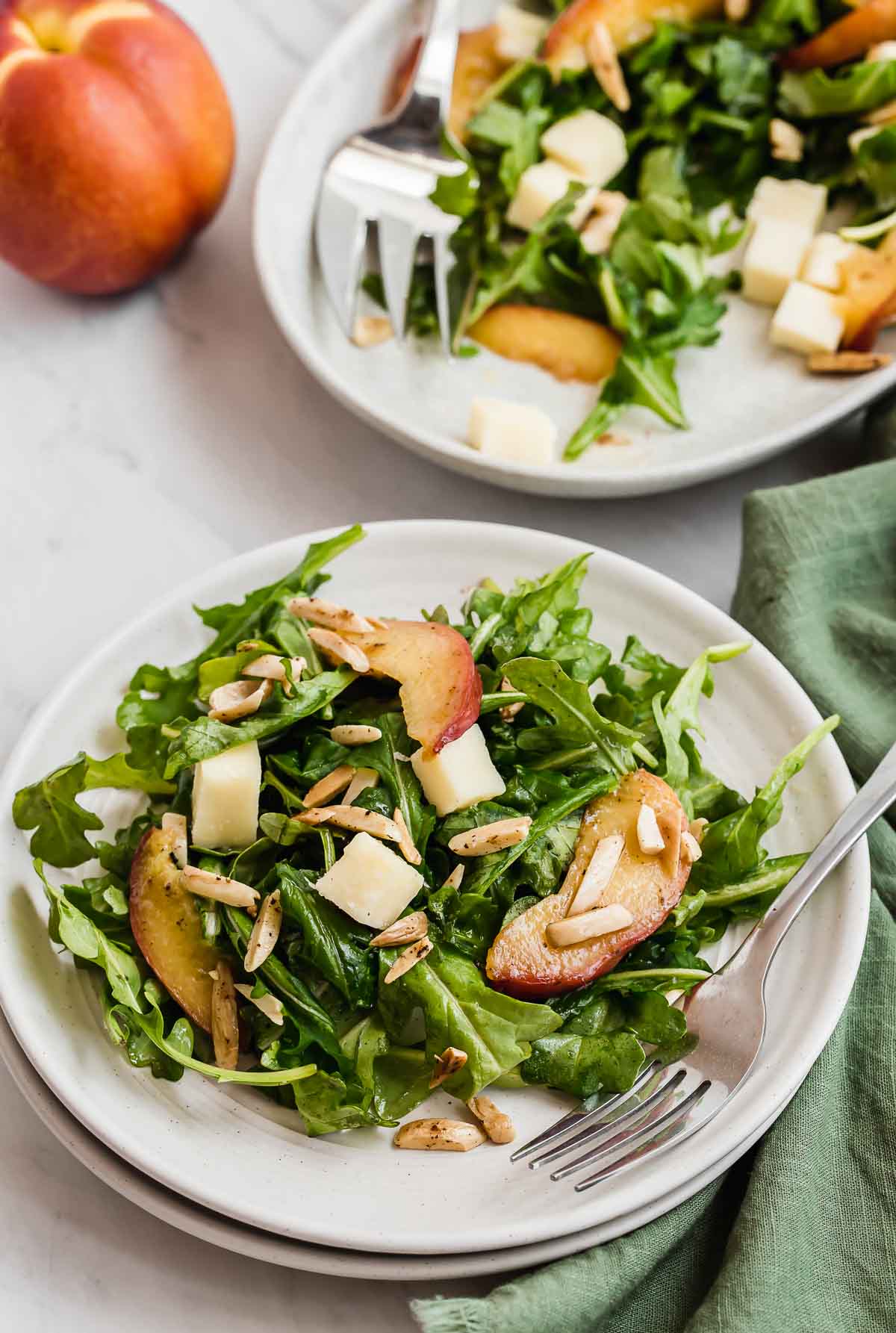 Two arugula salads on plates with nectarine in background.