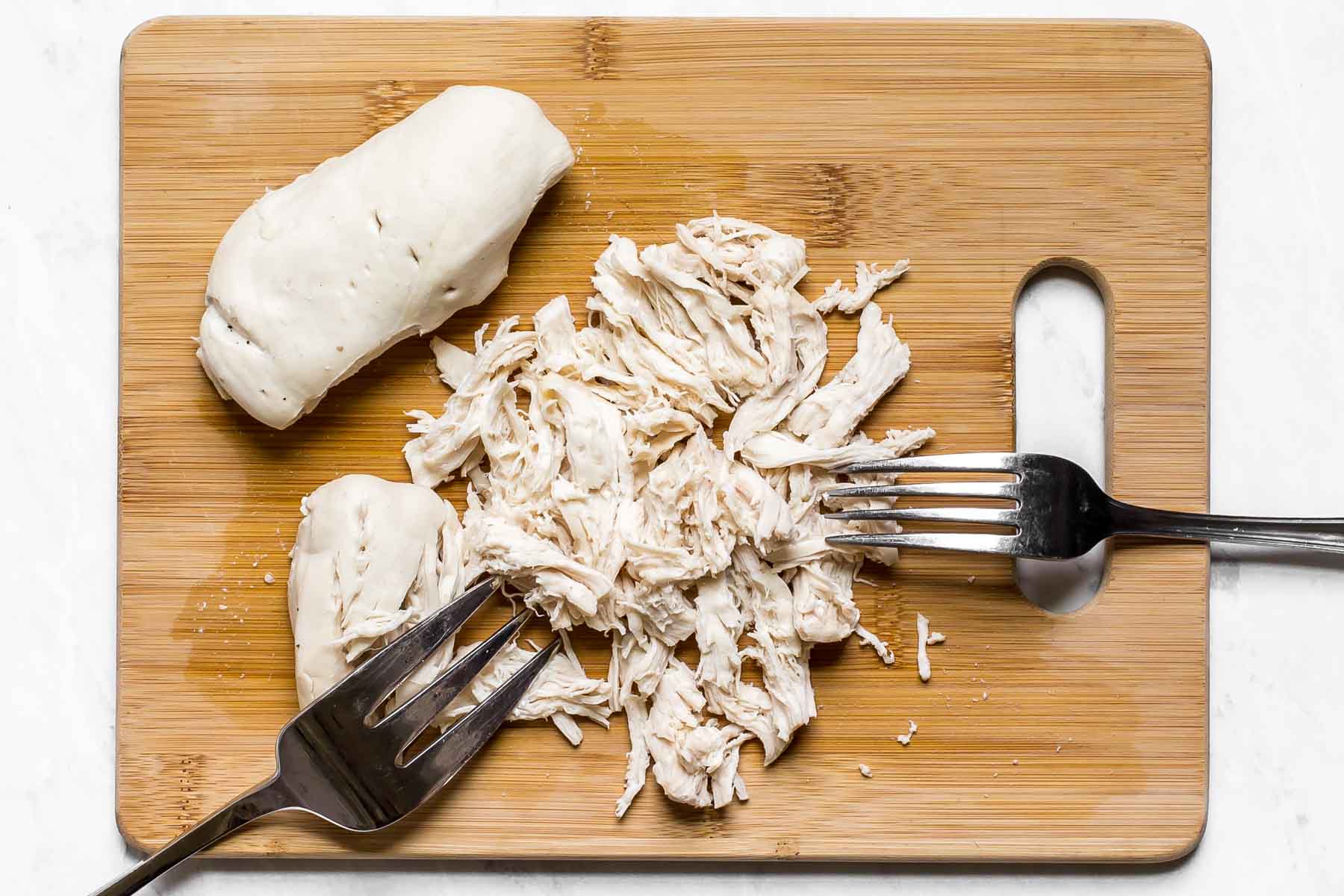 Shredded chicken on a wooden cutting board with two forks.