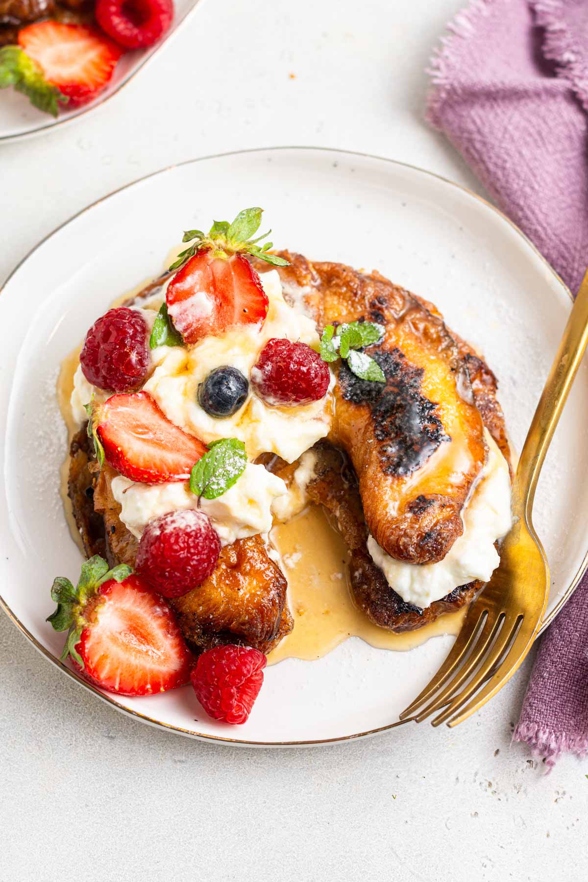 Croissant French toast on plate with berries and cream.