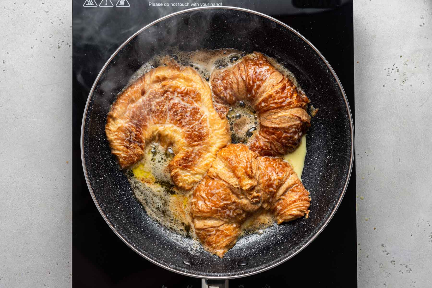 Croissants cooking in a skillet with butter.