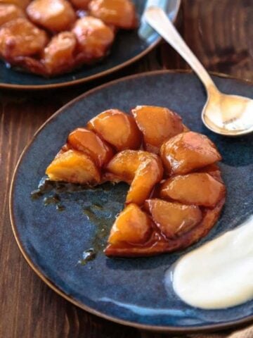 Two servings of apple tarte tatin on dark blue plates with cream dollop.
