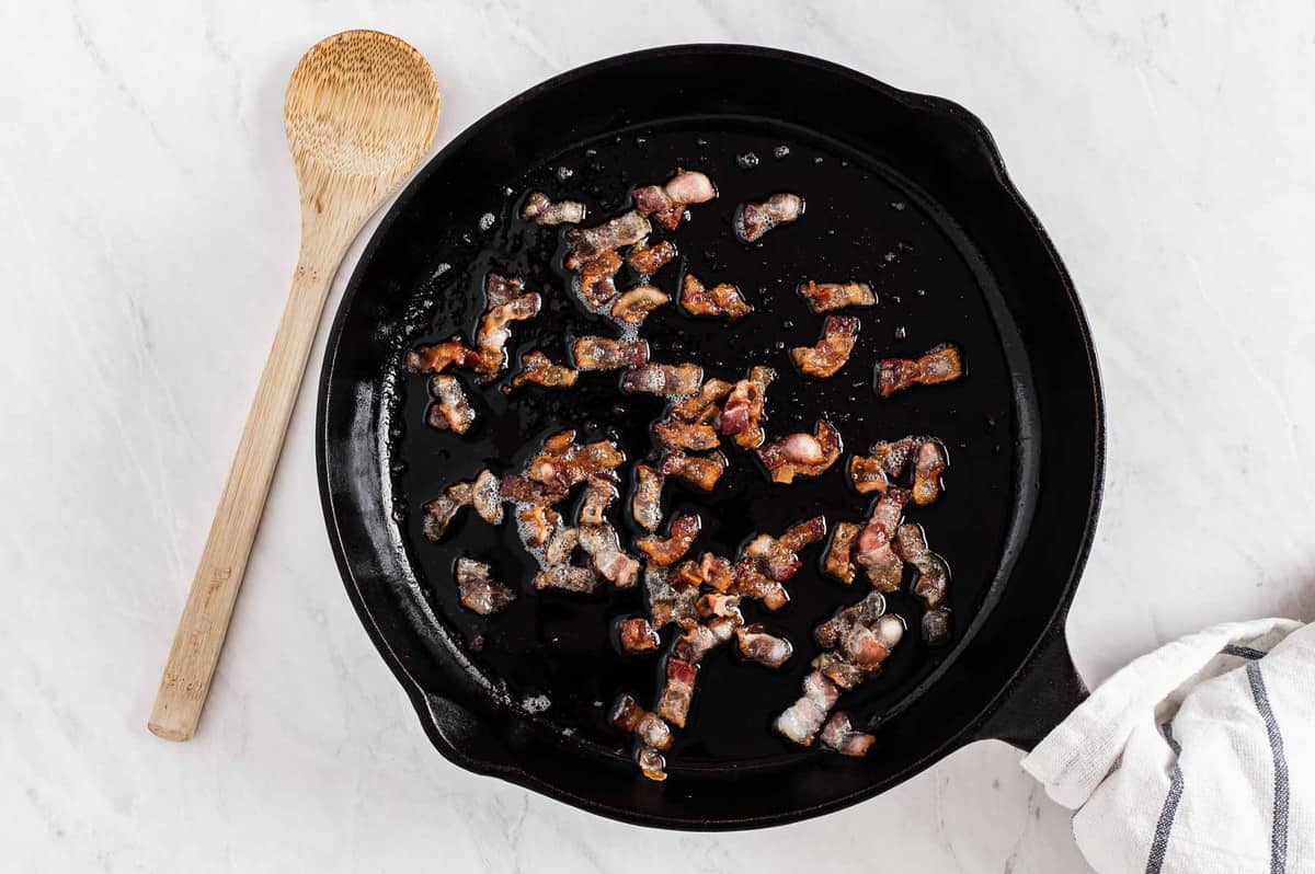 Bacon pieces cooking in a cast iron skillet.