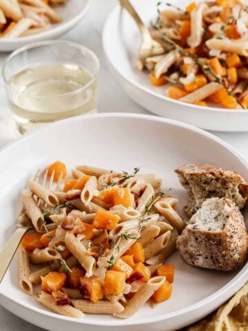 Two bowl of pasta with butternut squash cubes and bread on the side.