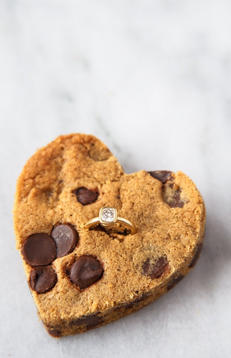 Chocolate Chip cookie cut into heart shape with diamond ring inserted.