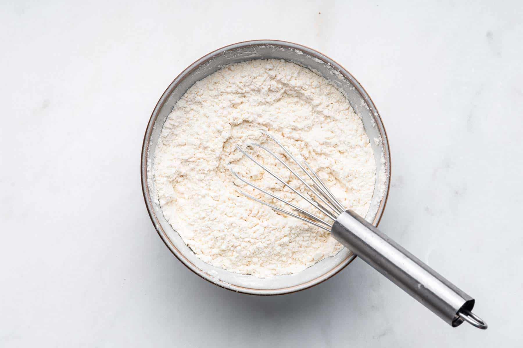 White bowl of flour with whisk.