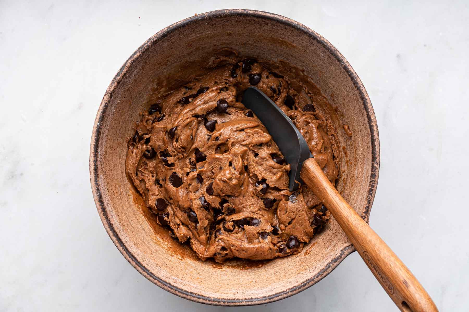 Dark brown dough in a brown bowl with grey spatula.