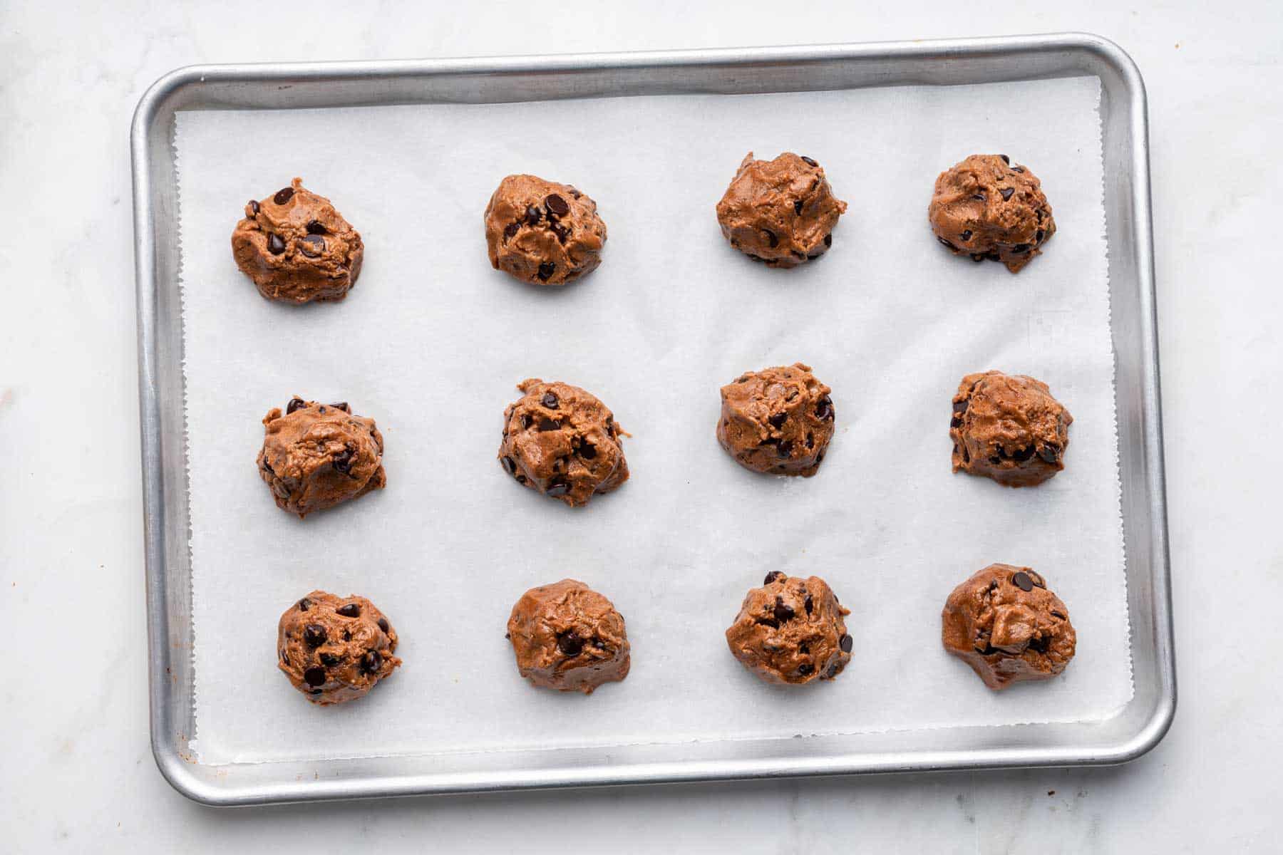 Twelve raw almond butter chocolate chip cookie dough balls on baking sheet.