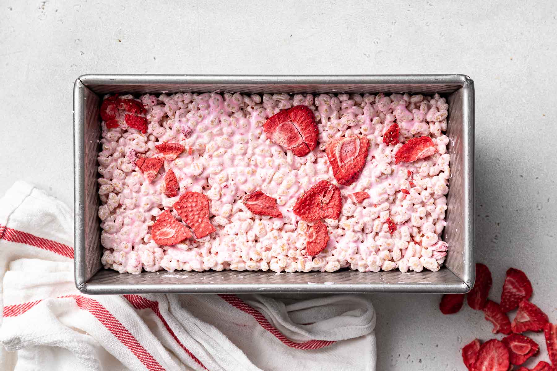 Pink Rice Krispie treats with strawberry slices on top in a loaf pan.