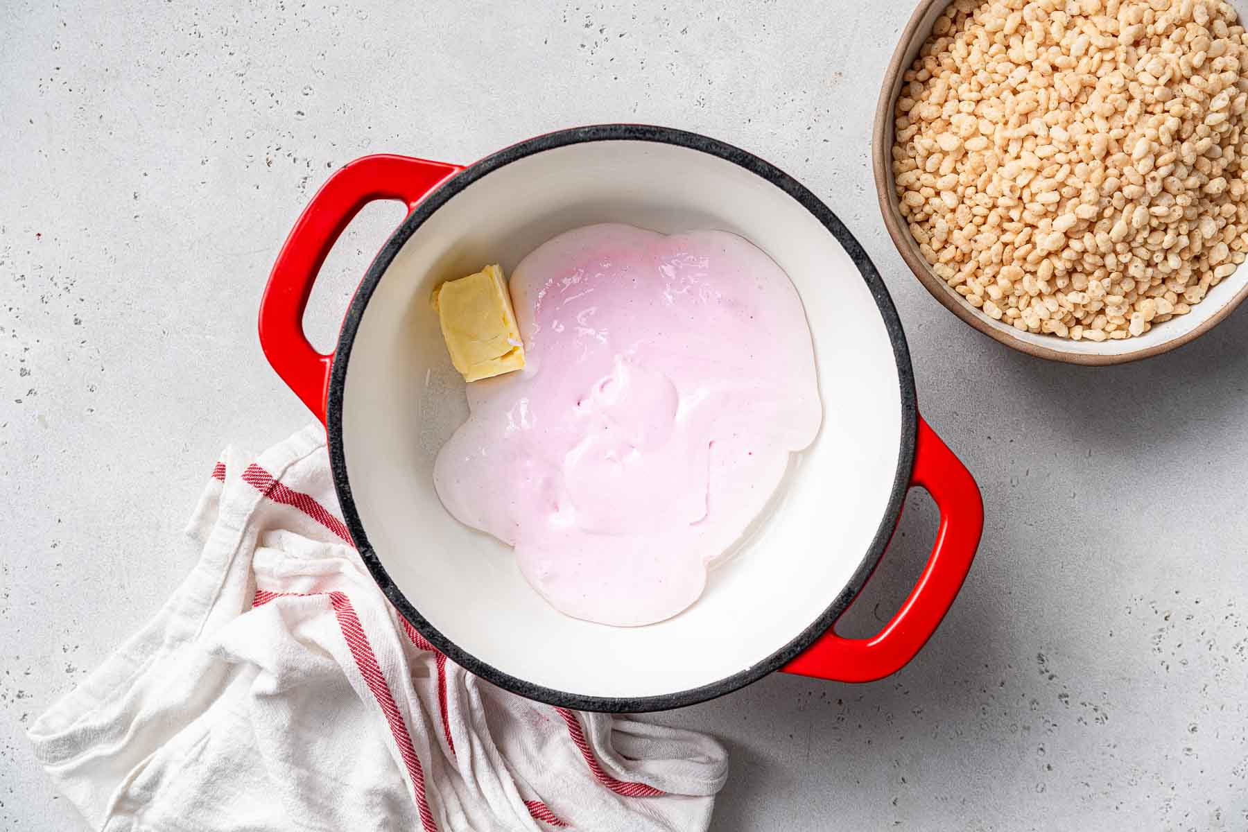 Pink melted marshmallows and butter in a red saucepan.