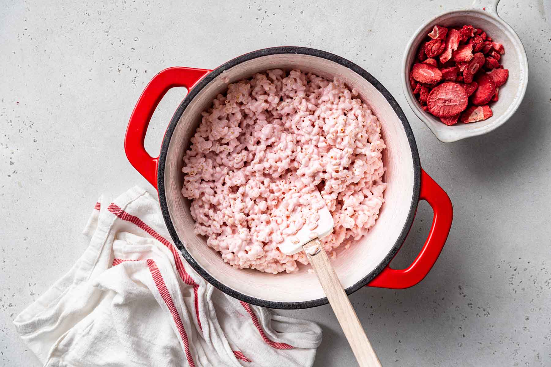 Stirring Rice Krispies cereal into pink melted marshmallows.