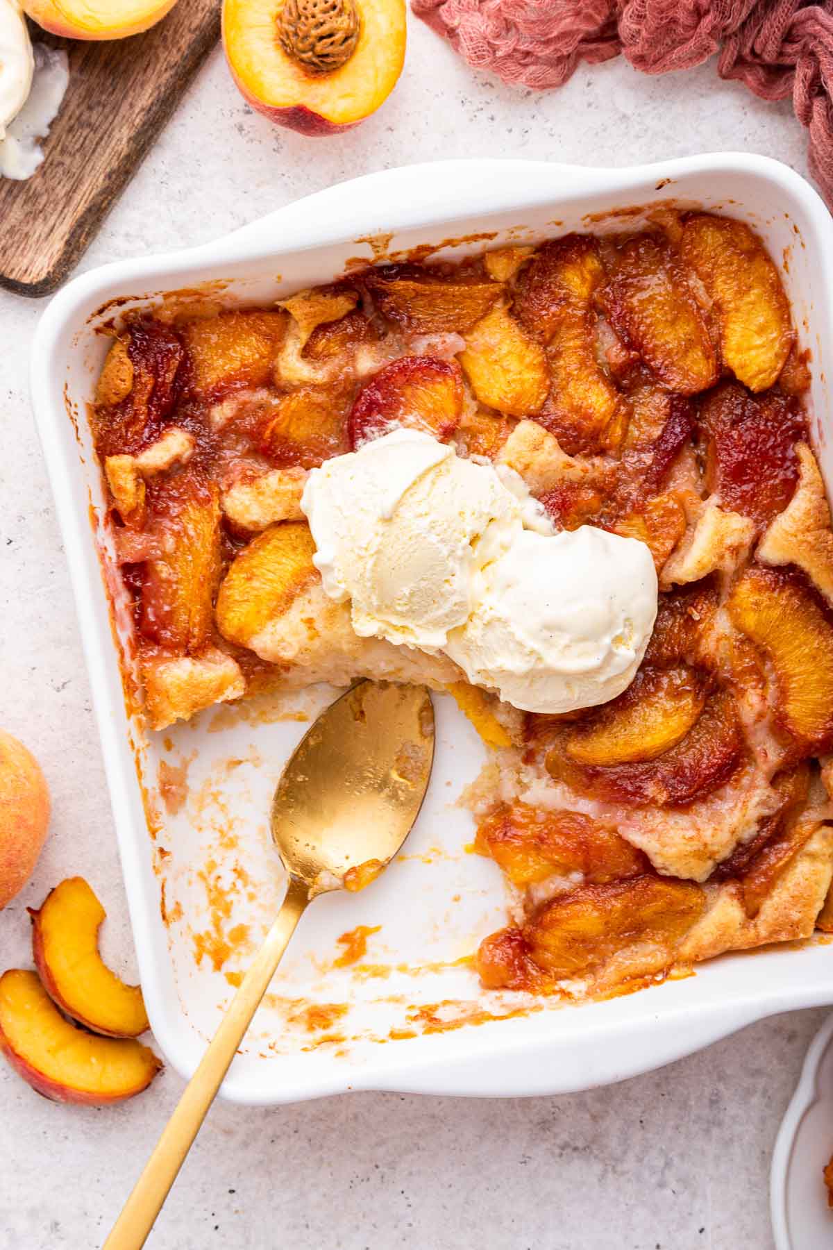 Fresh peach cobbler with a portion removed and gold spoon in empty space.