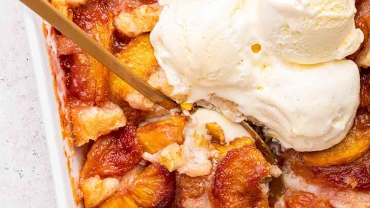 Fresh peach cobbler with scoops of vanilla ice cream on top in a square dish.