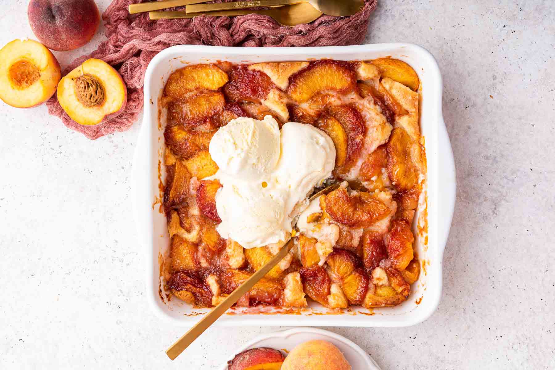 Freshly baked peach cobbler with 3 scoops of white vanilla ice cream on top and gold spoon.