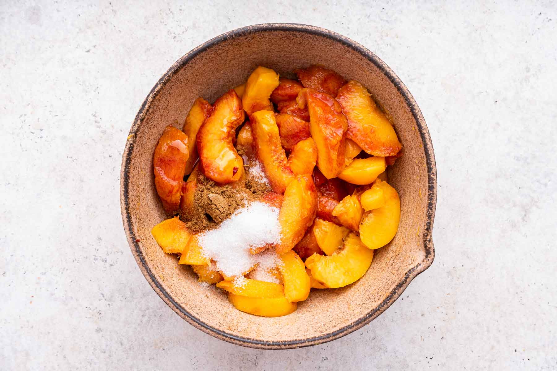 Bowl of sliced fresh peaches with sugar and cinnamon sprinkled on top.