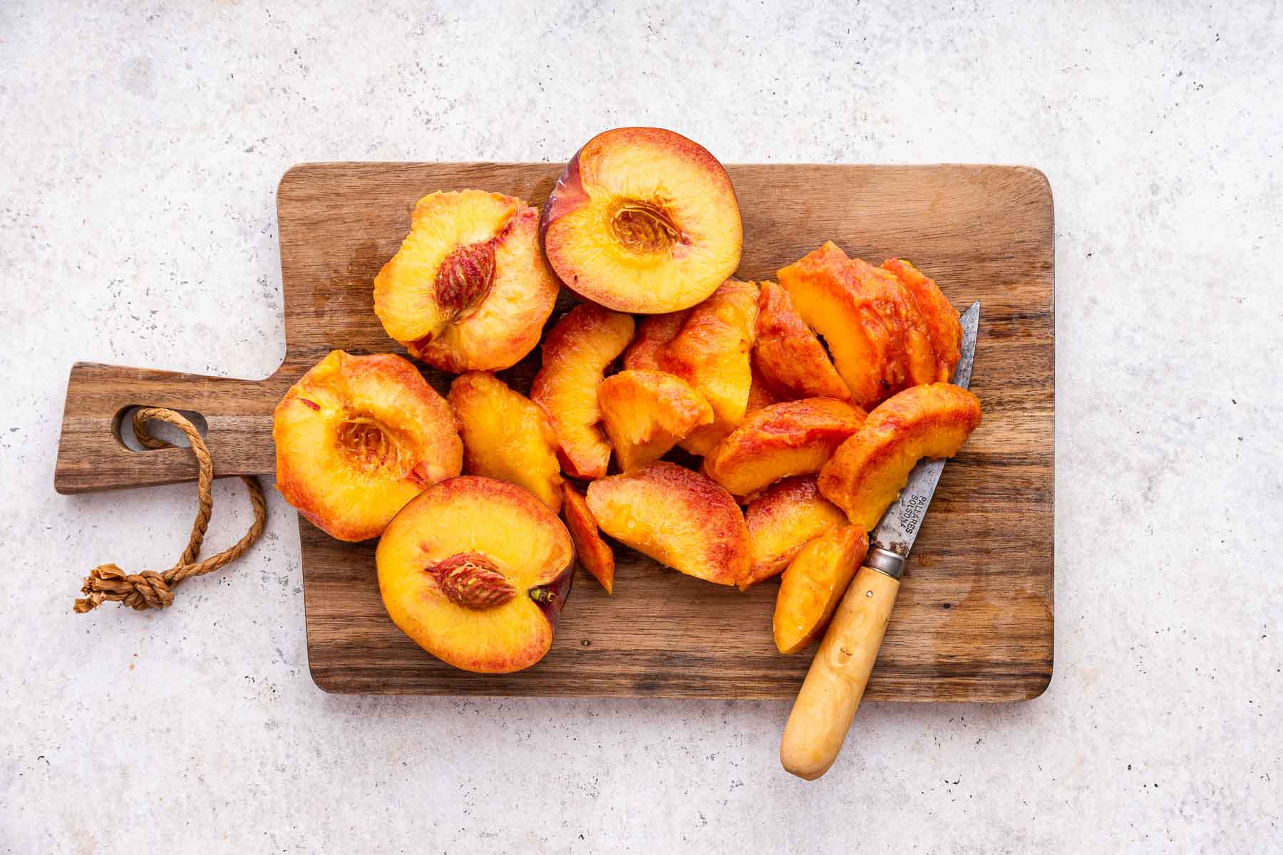 Fresh peaches being sliced on a wooden cutting board.