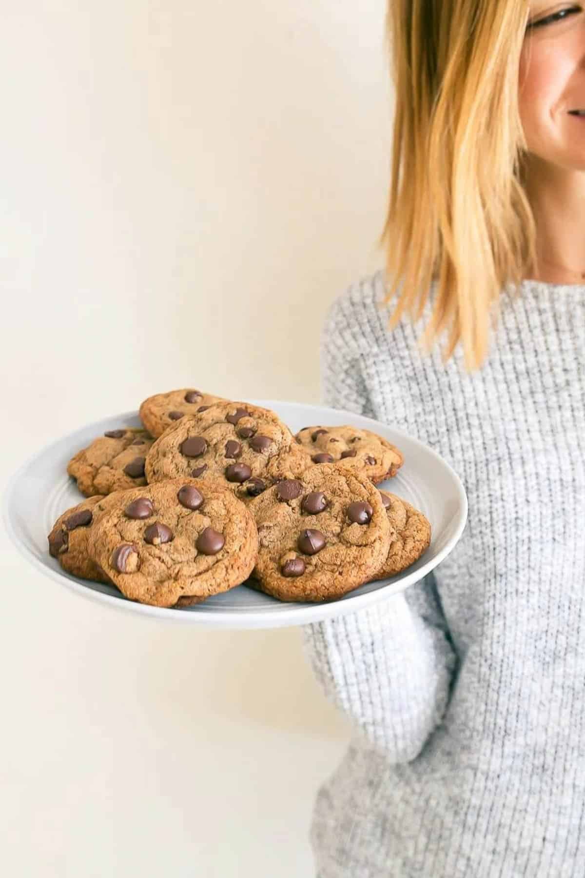 Woman with golden hair holding plate of healthy chocolate chip cookies.
