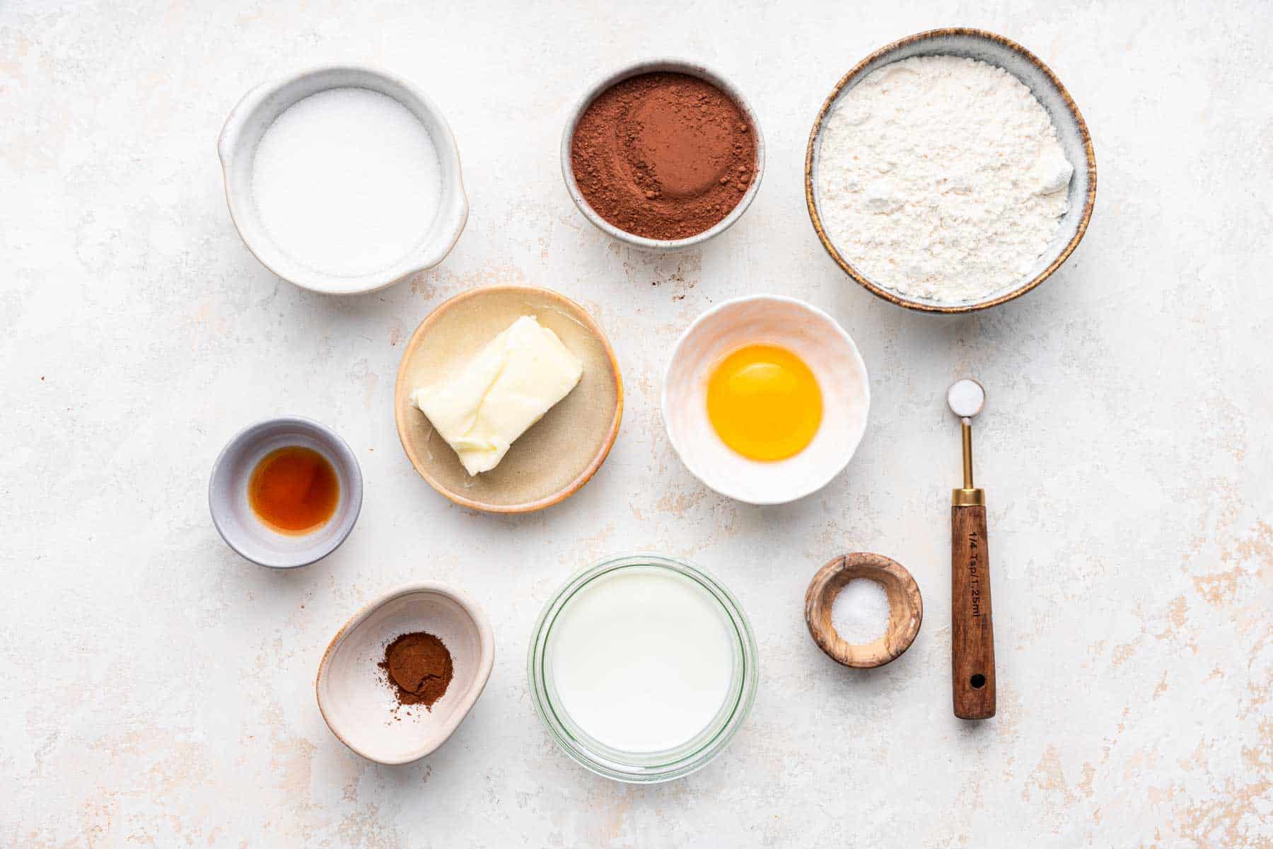 Small bowls of ingredients, including egg, cocoa powder, flour, and sugar on kitchen counter.