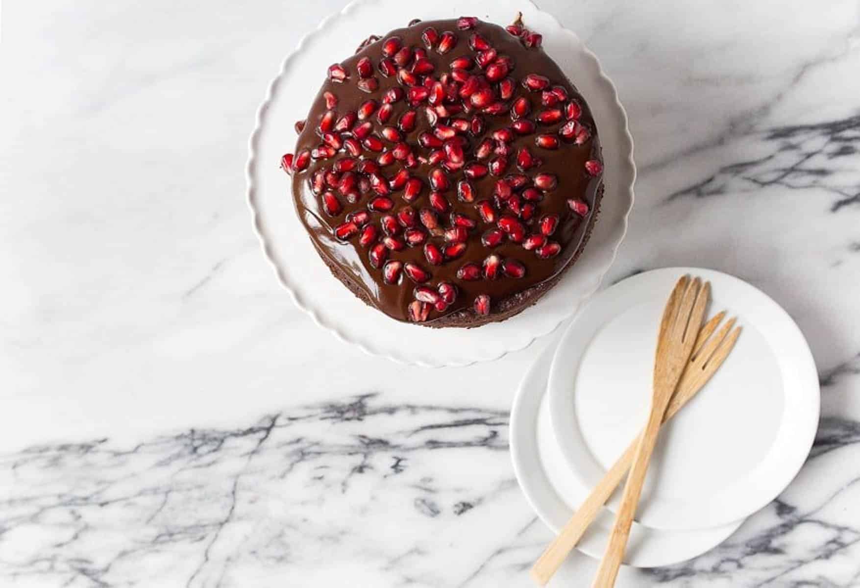 Overhead shot of small chocolate cake on white cake stand with pomegranate seeds on top.